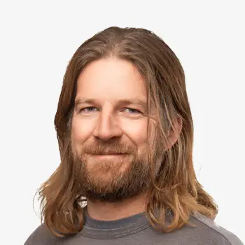 Happy man with long hair and beard smiling in casual gray T-shirt.