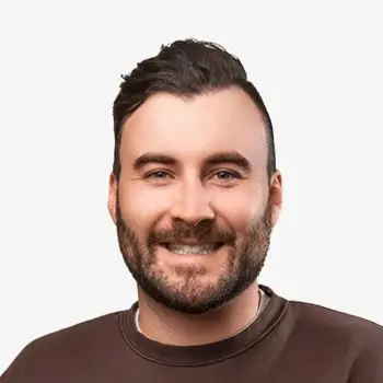 Smiling man with a beard and casual clothing, facing forward in a studio portrait.