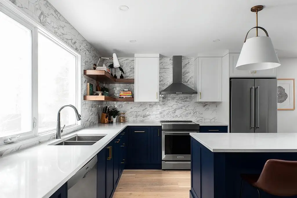 Bright modern kitchen with white marble countertops, navy blue cabinets, stainless steel appliances, and natural light.